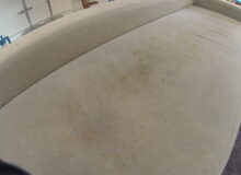 Zbliżenie na&nbsp;siedzisko jasnej, materiałowej kanapy, na&nbsp;której&nbsp;widoczne są&nbsp;rozległe, żółtawe i&nbsp;brązowawe plamy zabrudzeń. Stan mebla przed&nbsp;procesem czyszczenia.